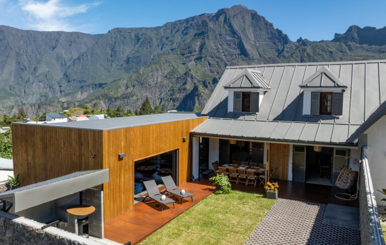Villa devant les montagnes, avec son jardin et deux transats. On voit l'entrée de la maison avec son parking privé.